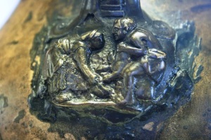 Attacco dell'ansa di un vaso di bronzo, con scena di sacrificio animale: un uomo (a dx) tiene un maiale e lo sgozza; una donna ne raccoglie il sangue con un catino. Provenienza pozzo Casini (foto del 16 maggio 2015).